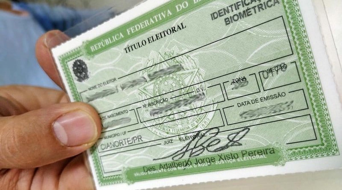 Mão segurando título eleitoral verde com dados pessoais e assinatura visíveis.