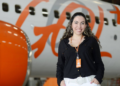Mulher com crachá da Gol sorrindo em frente a avião com logo da Gol em destaque