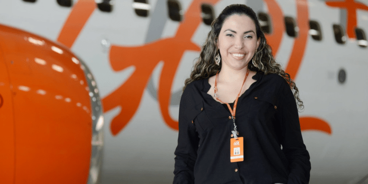 Mulher com crachá da Gol sorrindo em frente a avião com logo da Gol em destaque
