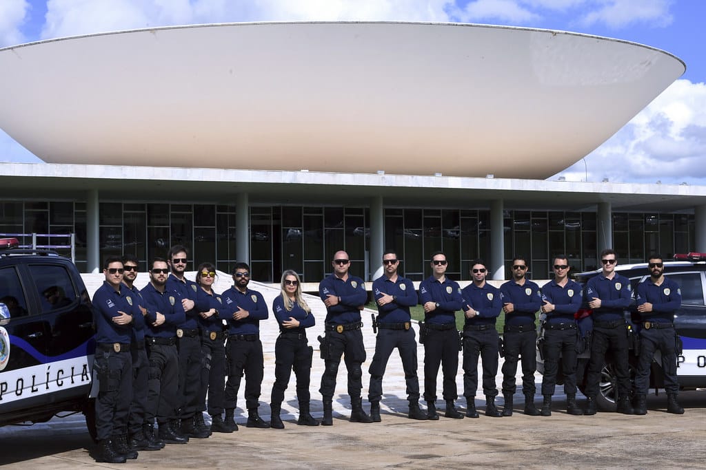 Grupo de policiais federais vestidos com uniforme azul escuro posando em frente ao Congresso Nacional, Brasília.