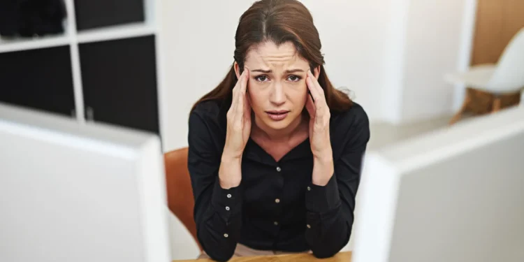 Mulher jovem e estressada, com expressão de frustração, sentada em sua mesa de trabalho, refletindo o estresse e arrependimento profissional após a graduação.