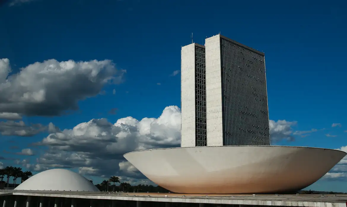 Câmara dos Deputados Imagem do prédio da Câmara dos Deputados, símbolo do poder legislativo em Brasília, com nuvens no céu.