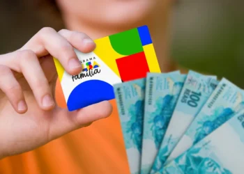 Cartão do Bolsa Família sendo segurado com notas de cem reais ao fundo sobre antecipação do pagamento de fevereiro em oito estados