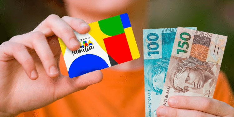 Mãos segurando cartão do Bolsa Família ao lado de notas de R$ 100 e R$ 150