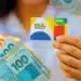 Cartão do Bolsa Família ao lado de cédulas de real, representando a antecipação do pagamento em fevereiro