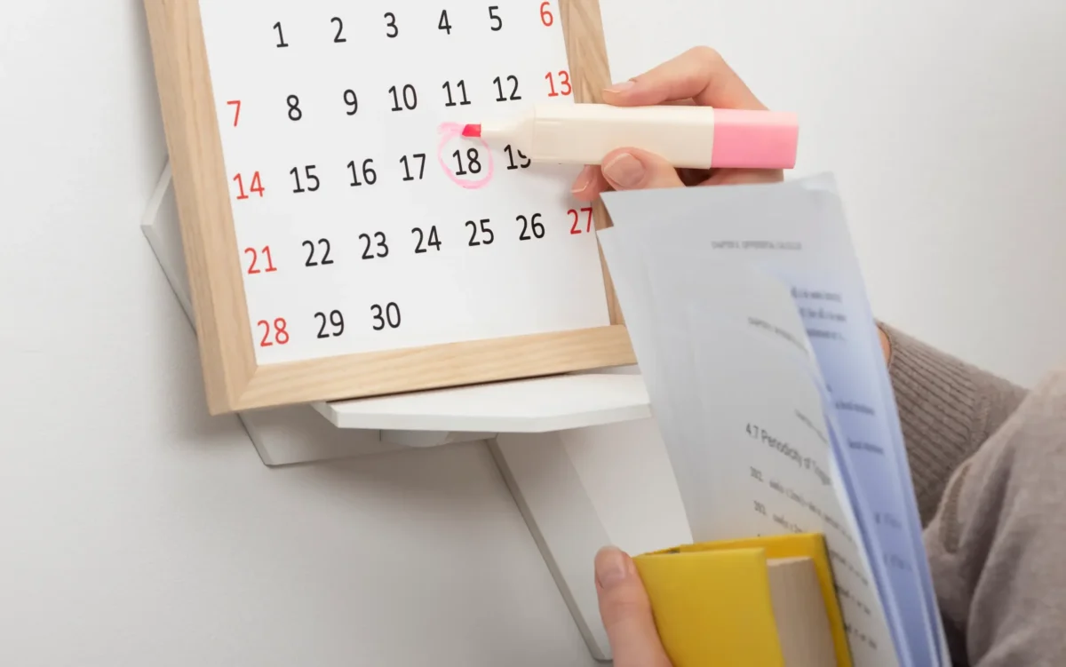 Governo divulga calendário oficial de feriados e pontos facultativos de 2026. Pessoa marcando data em calendário de parede representando a organização dos feriados nacionais e pontos facultativos de 2026.