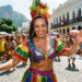 Mulher sorridente com fantasia colorida e adereço de frutas dança em bloco de Carnaval nas ruas.