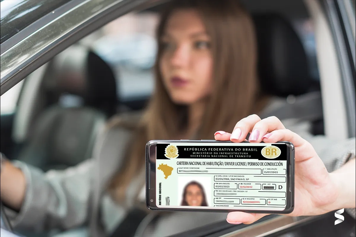 CNH Social Governo do Paraná – Quem pode participar Mulher dentro de carro exibindo CNH digital no celular como referência ao programa CNH Social do Governo do Paraná