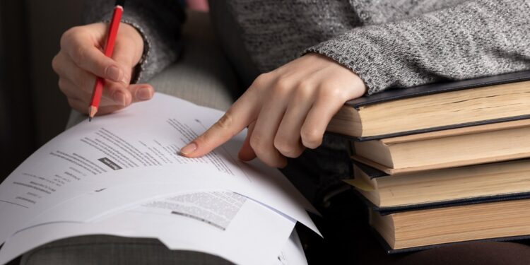 Pessoa estudando com livros e fazendo anotações em papel para concurso público