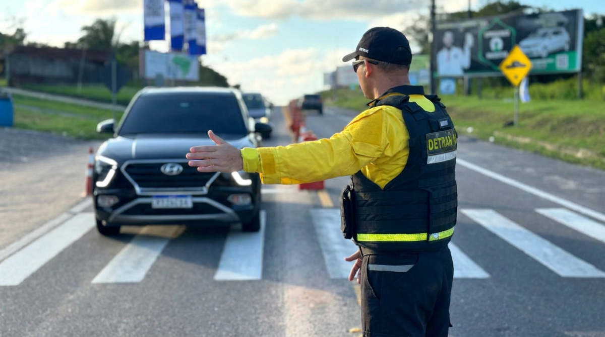 Concurso Detran 2026 Agente do DETRAN sinaliza para carro preto parar em blitz na faixa de pedestre