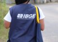 Recenseador do IBGE caminha em rua de bairro com colete azul e bolsa institucional