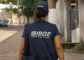 Recenseador do IBGE caminhando em rua residencial com uniforme durante coleta de dados para o Censo Agropecuário, Florestal e Aquícola.
