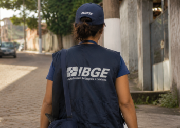 Recenseador do IBGE caminhando em rua residencial com uniforme durante coleta de dados para o Censo Agropecuário, Florestal e Aquícola.
