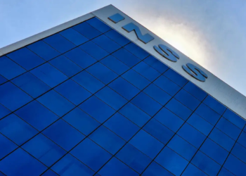 Prédio envidraçado do INSS refletindo o céu com letreiro visível no topo