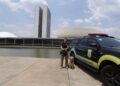 Policial legislativa federal com cão farejador ao lado de viatura em frente ao Congresso Nacional em Brasília