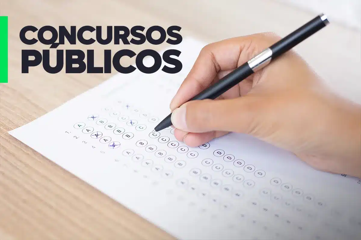 Processo Seletivo Prefeitura de Almenara-MG 2026 Mão segurando caneta sobre gabarito de prova de múltipla escolha com o texto "Concursos Públicos" em destaque