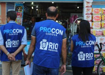 Três fiscais do Procon RJ vistoriando comércio com coletes azuis em frente a farmácia