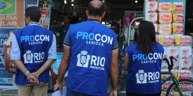 Três fiscais do Procon RJ vistoriando comércio com coletes azuis em frente a farmácia