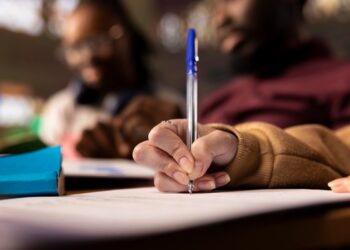 Mão segurando caneta escrevendo em documento representando candidato de concurso público