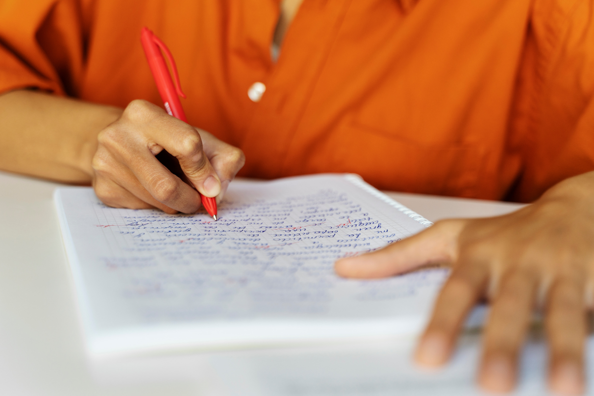 Concursos Prefeituras 2026 Pessoa escreve de caneta vermelha em caderno com anotações manuscritas