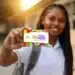 Jovem segurando cartão colorido do programa Pé-de-Meia com uniforme escolar e mochila