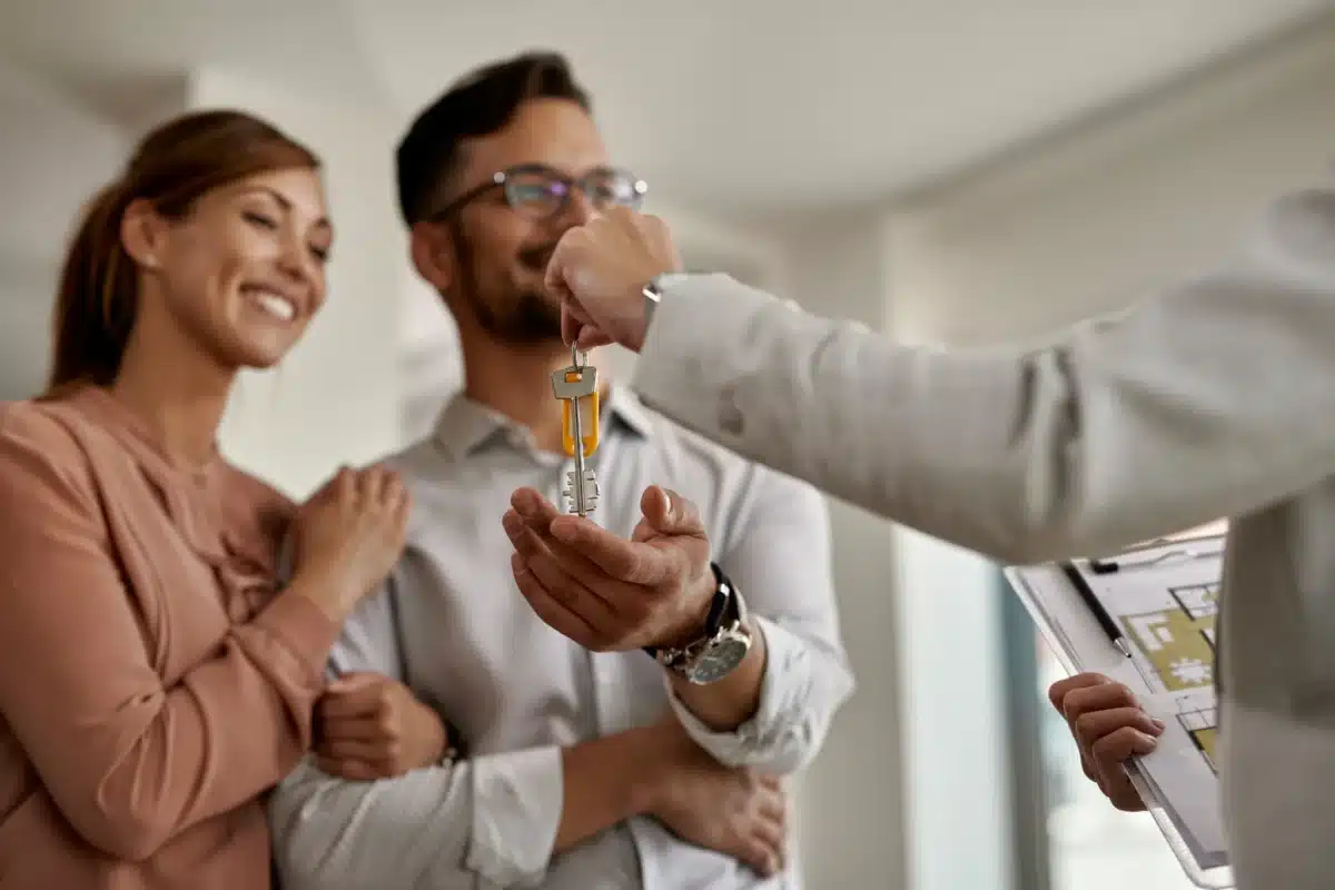 Corretor de imóveis especializado pode alcançar altos ganhos sem precisar de diploma universitário. Casal recebendo a chave de um imóvel novo de corretor, simbolizando carreira de corretor de imóveis especializado sem faculdade.