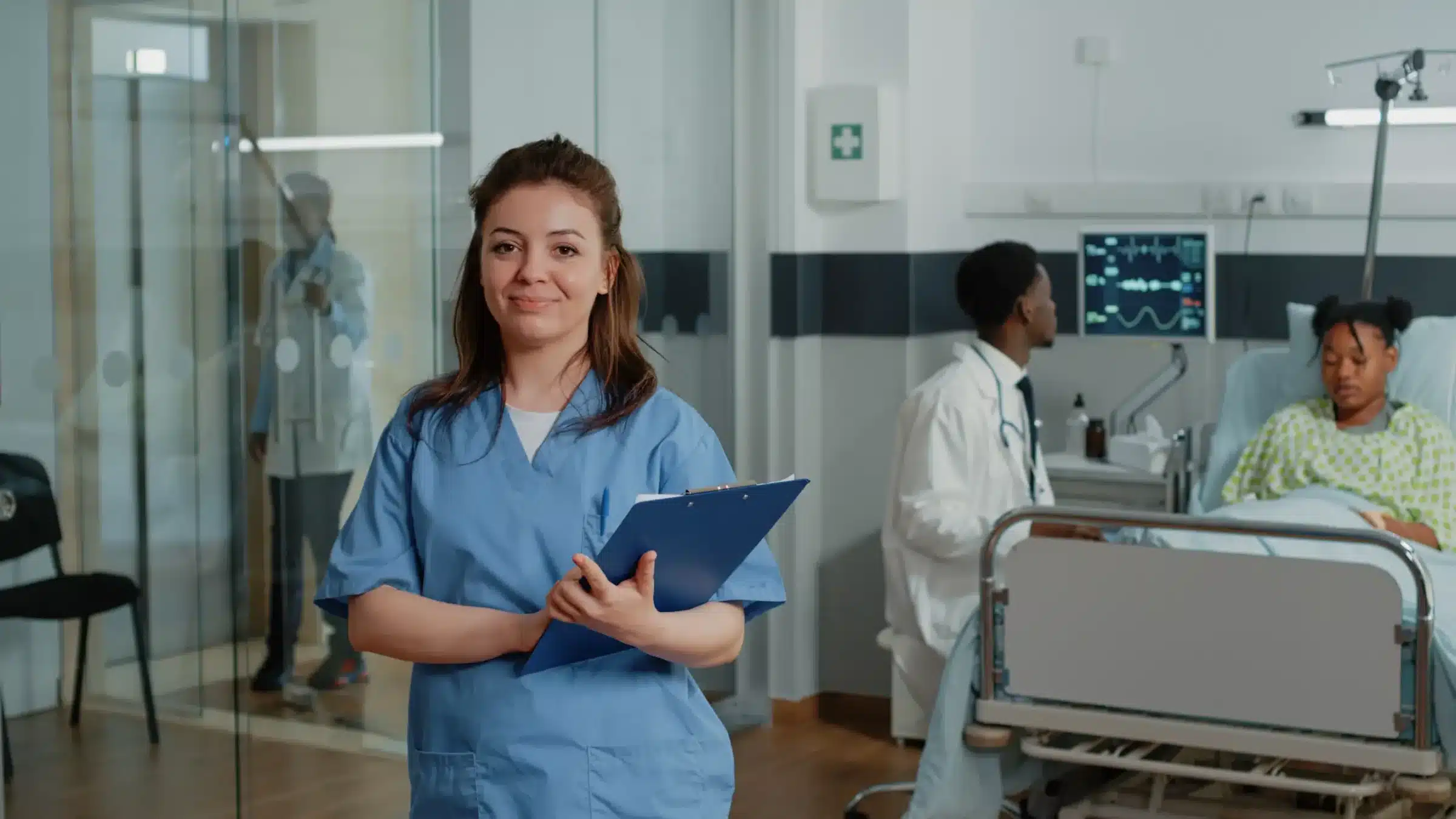 Técnico de Enfermagem Profissional de saúde sorrindo em ambiente hospitalar com paciente em atendimento.