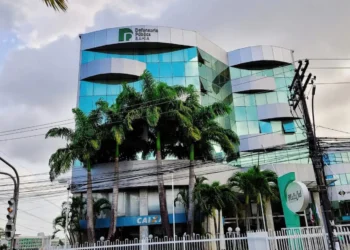 Prédio da Defensoria Pública do Estado da Bahia (DPE-BA), com o logo visível na parte superior, rodeado por palmeiras e infraestrutura urbana ao redor.