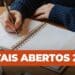 Pessoa escrevendo com caneta em agenda aberta marcada com datas de 2026