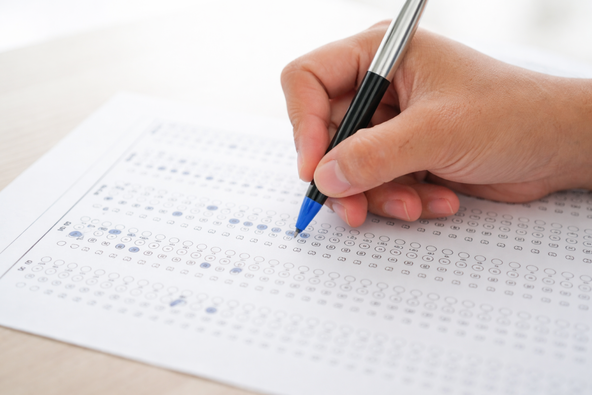 Editais abertos 2026 Mão segurando caneta azul marca respostas em folha de prova objetiva