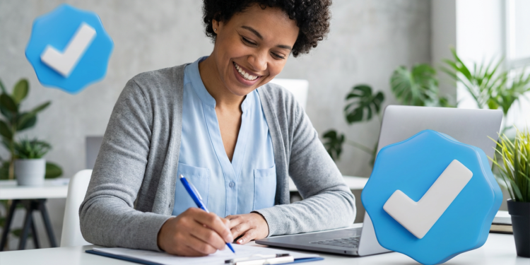 Mulher sorridente escrevendo em prancheta ao lado de notebook e ícones de verificação azul