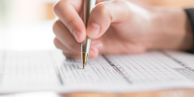 Pessoa escrevendo com caneta dourada em formulário impresso sobre mesa de madeira