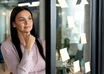 Mulher pensativa refletindo sobre escolha de carreira e profissão com post-its de planejamento ao lado