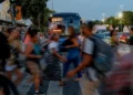 Grupo de trabalhadores atravessa faixa com ônibus e veículos ao fundo ao anoitecer