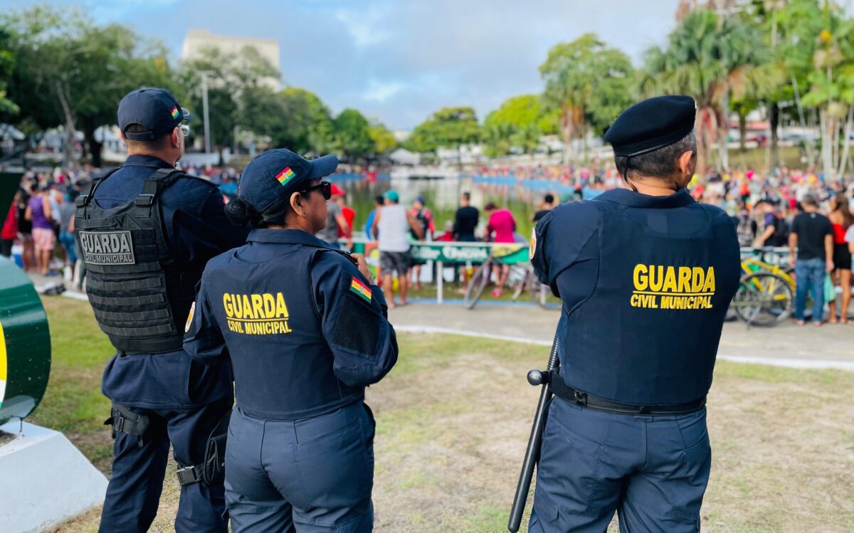 Guarda Municipal Três guardas civis municipais observam multidão durante evento ao ar livre próximo a lago