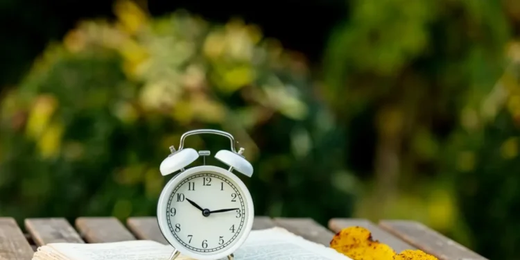 Relógio de alarme sobre livro com folhas de outono, representando o possível horário de verão 2026 no Brasil
