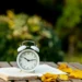 Relógio de alarme sobre livro com folhas de outono, representando o possível horário de verão 2026 no Brasil