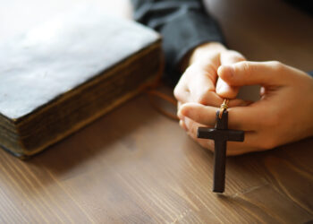 Imagem de mãos segurando um crucifixo e uma Bíblia sobre uma mesa de madeira, simbolizando a fé cristã durante a Quaresma.