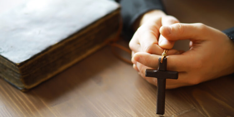 Imagem de mãos segurando um crucifixo e uma Bíblia sobre uma mesa de madeira, simbolizando a fé cristã durante a Quaresma.