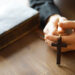 Imagem de mãos segurando um crucifixo e uma Bíblia sobre uma mesa de madeira, simbolizando a fé cristã durante a Quaresma.