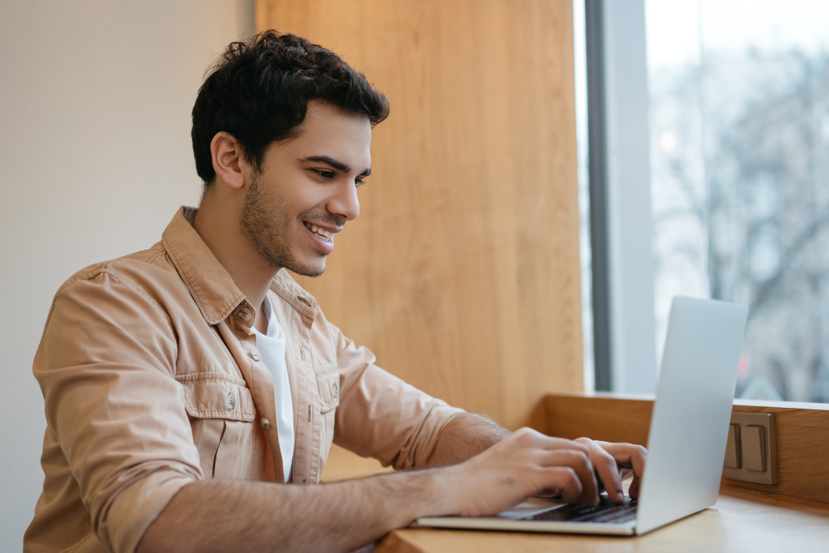 Inscrição Prefeitura Rapaz sorrindo utiliza notebook próximo à janela em ambiente de estudos