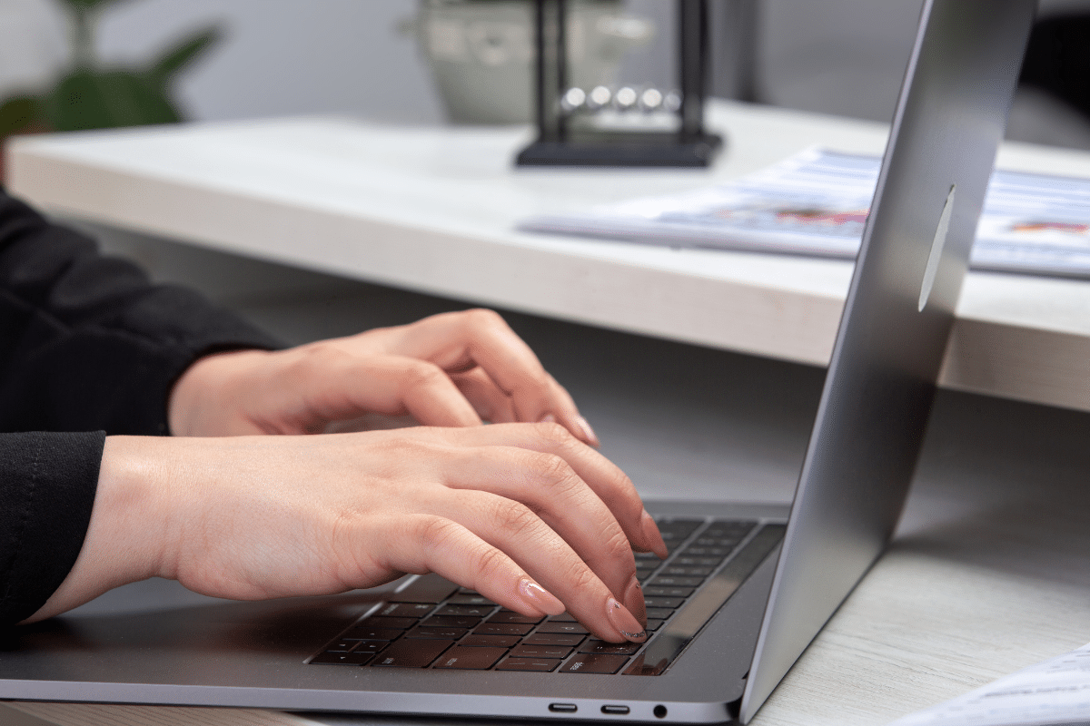 Mãos femininas digitando em notebook sobre mesa branca com documentos