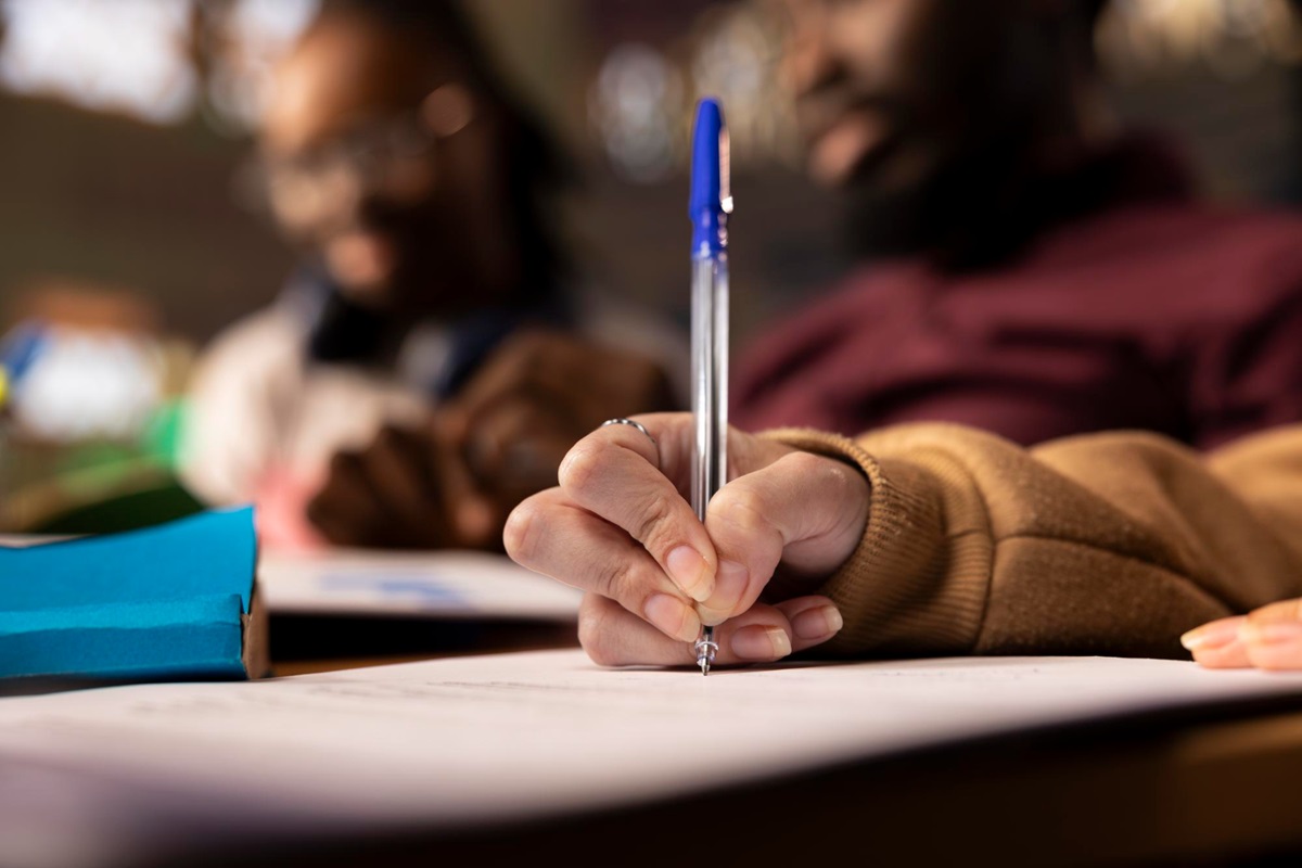 Inscrições concurso Prefeitura Jacobina BA 2026 prazo final domingo Mão segurando caneta azul escrevendo em folha de papel durante inscrição para concurso
