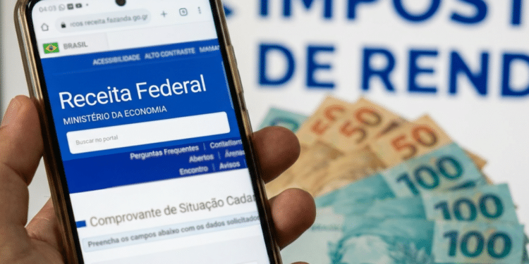 Pessoa acessando site da Receita Federal no celular, com cédulas de dinheiro ao fundo.