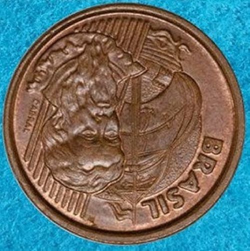 erros cunhagem moeda 1 centavo reverso invertido Close de uma moeda de 1 centavo de cobre apresentando erro de reverso invertido. A face exibida mostra a efígie de Pedro Álvares Cabral e a nau de cabeça para baixo em relação à posição padrão de cunhagem. A moeda está sobre um fundo azul texturizado.