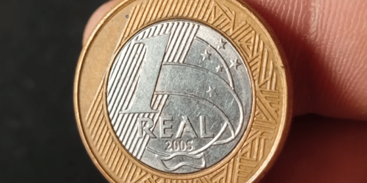 Close de uma moeda de 1 real do ano de 2005, com foco na data gravada na base dourada e no rosto da República no centro prateado.
