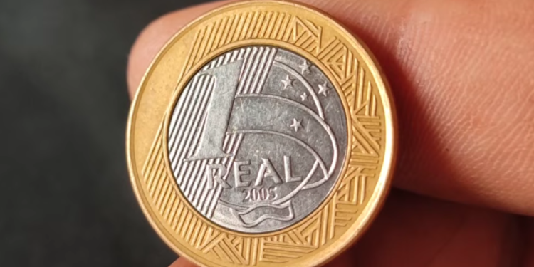 Close-up do anverso de uma moeda de 1 real comemorativa dos 40 anos do Banco Central (2005). O centro prateado exibe o prédio do Banco Central e a sigla BC, enquanto o anel dourado contém a legenda "BANCO CENTRAL DO BRASIL" e as datas "1965 40 ANOS 2005".