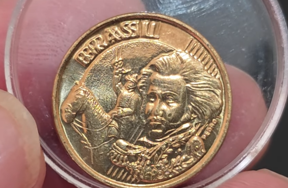 Close do reverso de uma moeda de 10 centavos do Real, mostrando a efígie de Dom Pedro I a cavalo e a palavra "BRASIL" ligeiramente duplicada, indicando um erro de cunho.