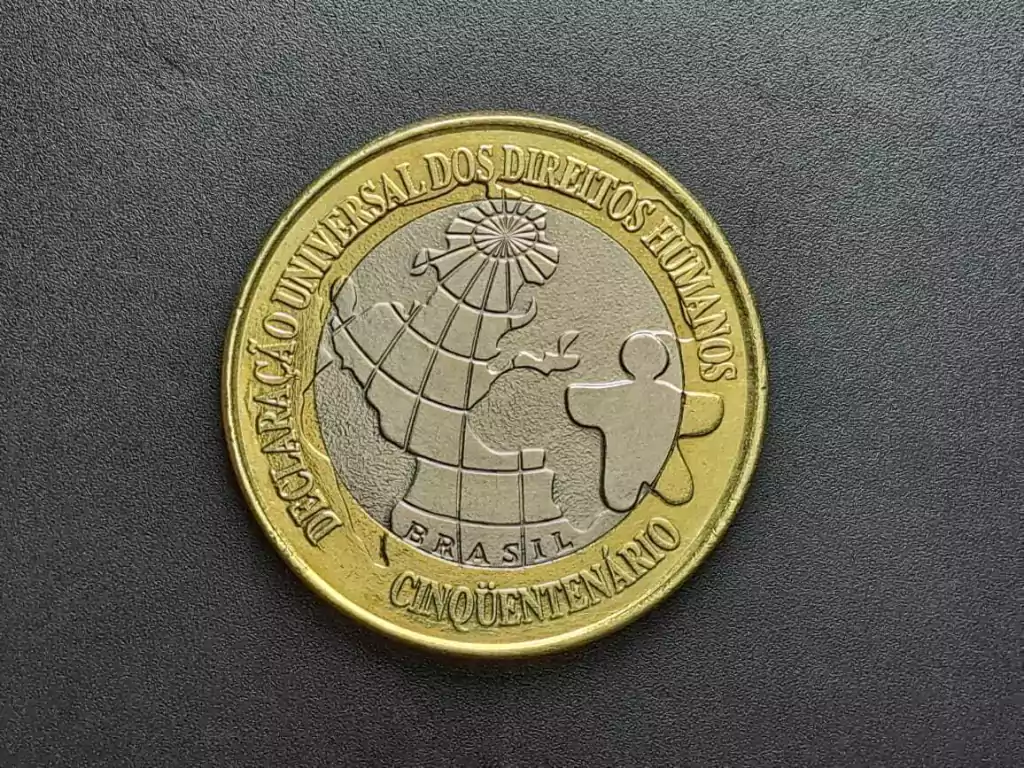 moeda 1 real direitos humanos 1998 valorizada Moeda de 1 Real comemorativa de 1998 sobre fundo escuro. Apresenta o desenho do globo terrestre e a figura humana estilizada, com a inscrição "Declaração Universal dos Direitos Humanos - Cinquentenário".