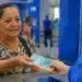 Aposentada recebe cédulas de real durante atendimento em uma agência bancária, representando os pagamentos de até R$ 8.475,55 previstos para julho.